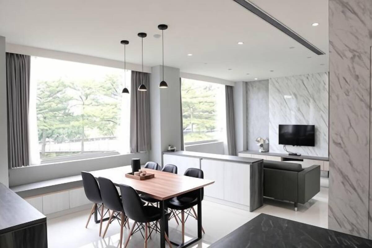 A modern dining area with a wooden table, black chairs, pendant lights, a TV, and a marble wall.