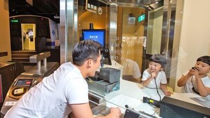 A man sitting at a counter with a computer and a phone, with a reflection of a child in the mirror. - Beitou Resort Metro Inn (Taipei)