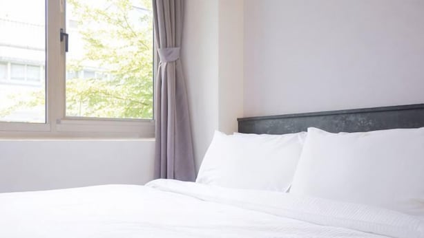 A neatly made bed with white linens in a room with a window and a curtain. - Beitou Resort Metro Inn (Taipei)