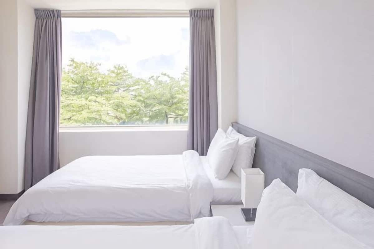 A hotel room with a bed, a bedside table, and a window with curtains.