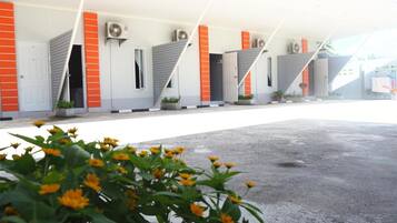 A row of hotel rooms with air conditioning units, a covered outdoor area, and a paved entrance.