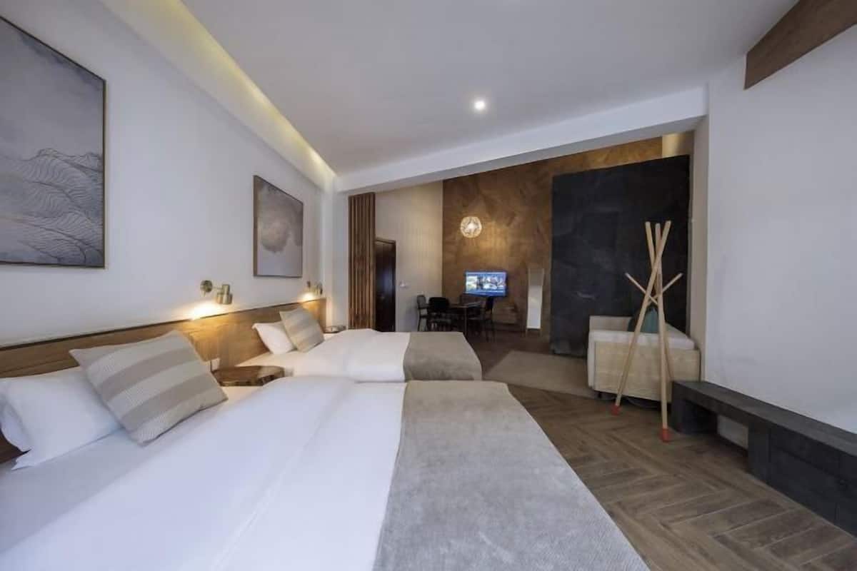A hotel room with two beds, a desk, a TV, and a fireplace.