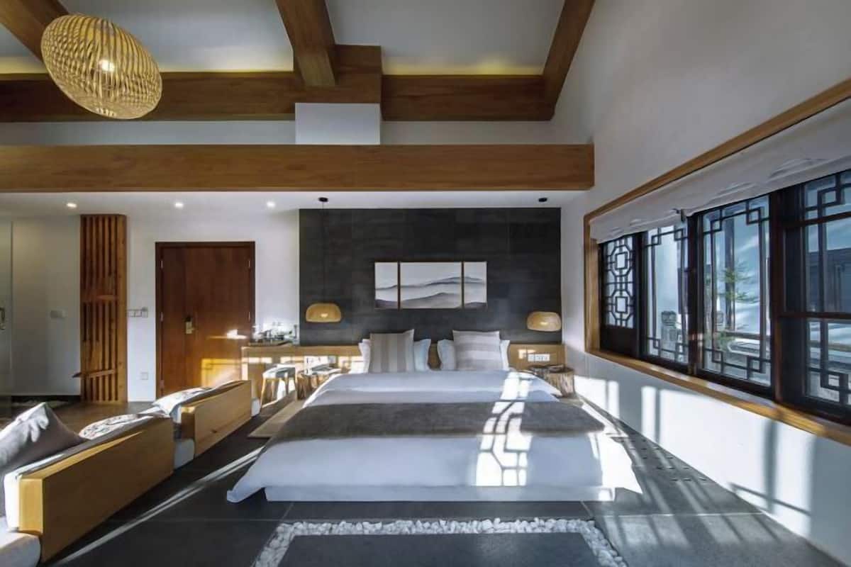 A modern bedroom with a large bed, wooden beams, a large window, and a view of the outdoors.