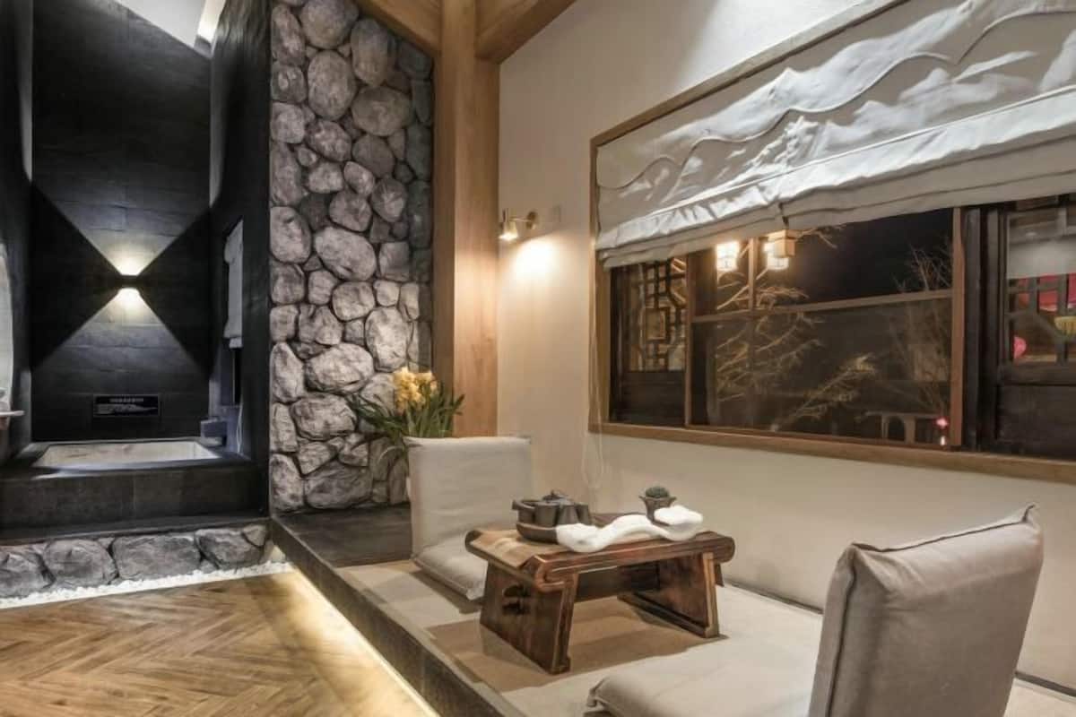 A room with a stone wall, a fireplace, a wooden bench, and a window with a view of trees.