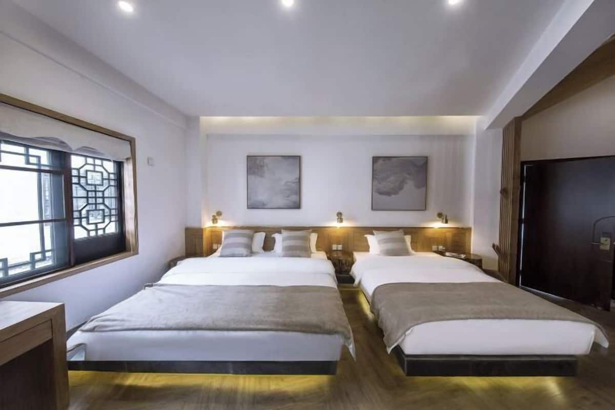 A hotel room with two beds, a large window with a geometric design, and artwork on the walls.