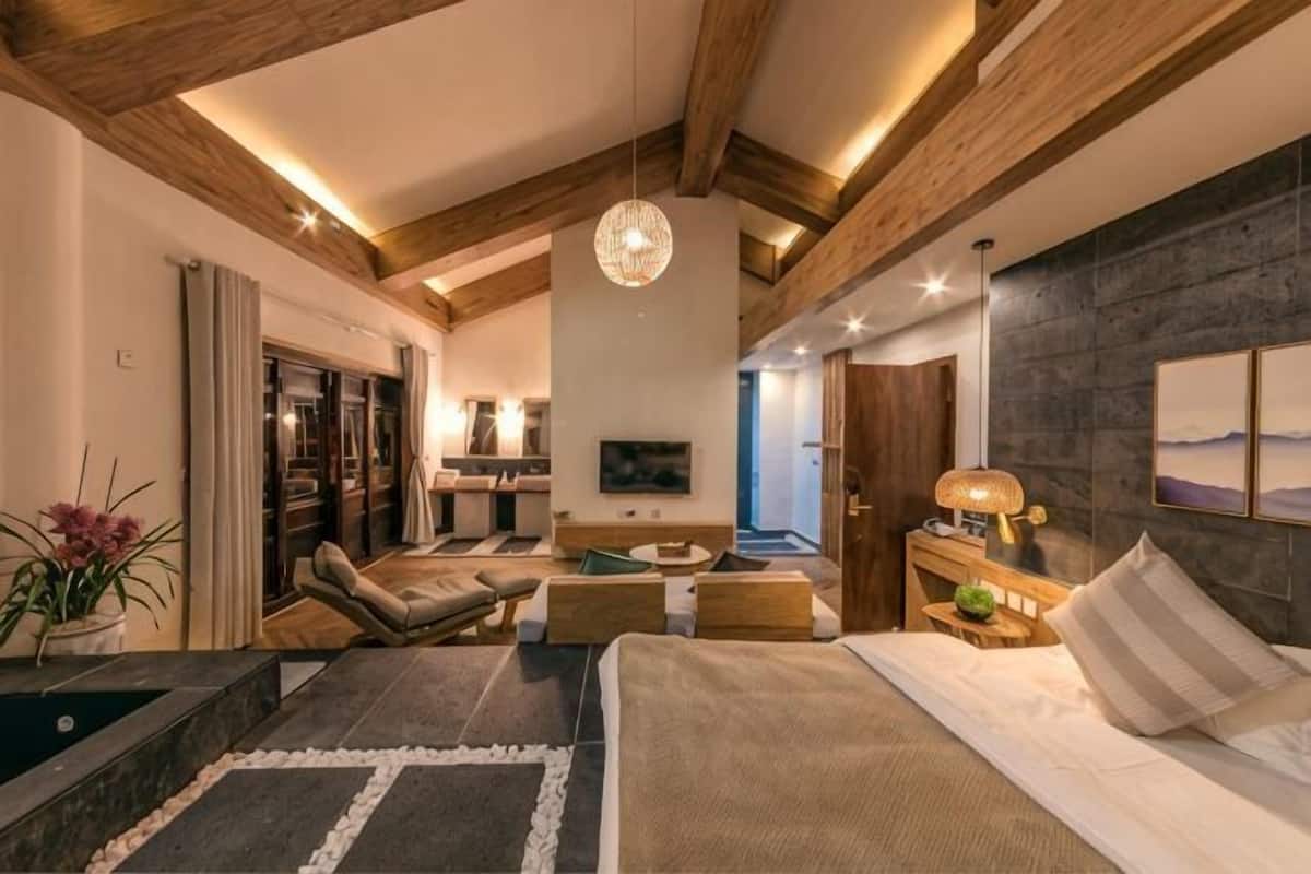 A spacious bedroom with a large bed, a seating area with a sofa and chairs, a TV, and a wooden ceiling.