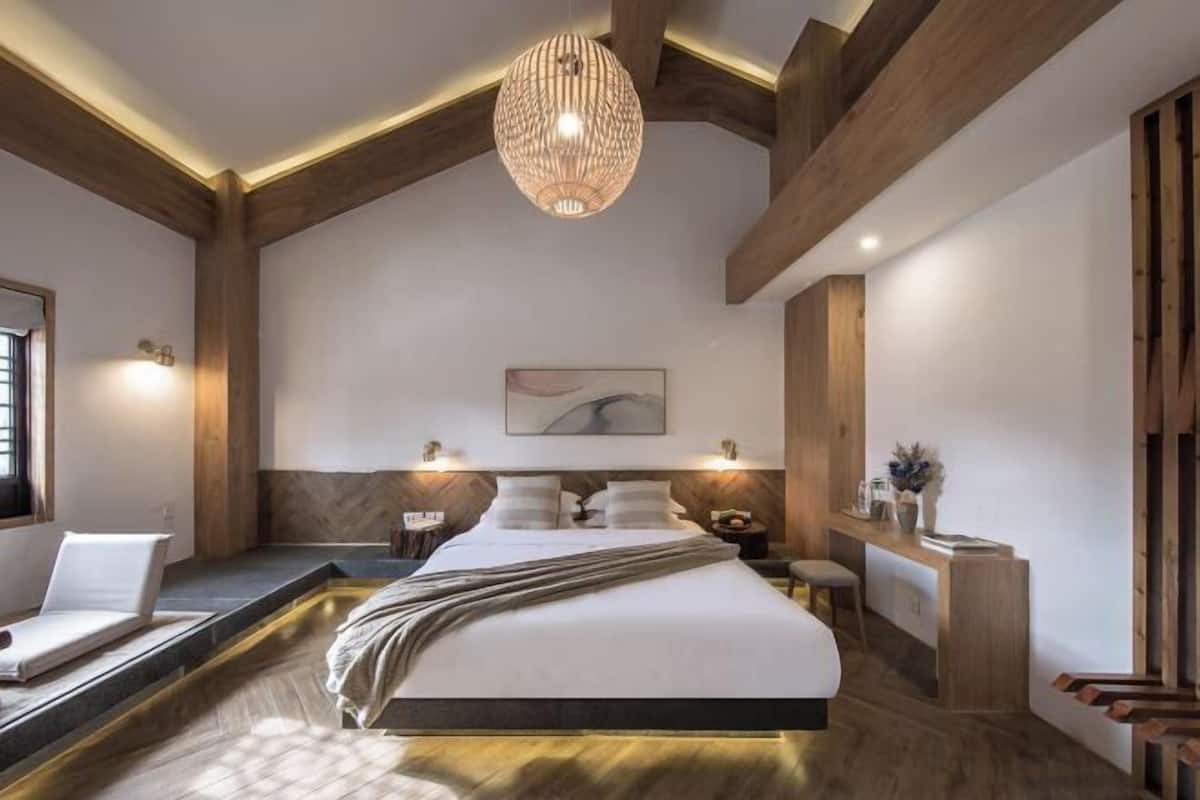 A modern bedroom with a large bed, wooden beams, a hanging light fixture, and a bedside table with a vase.