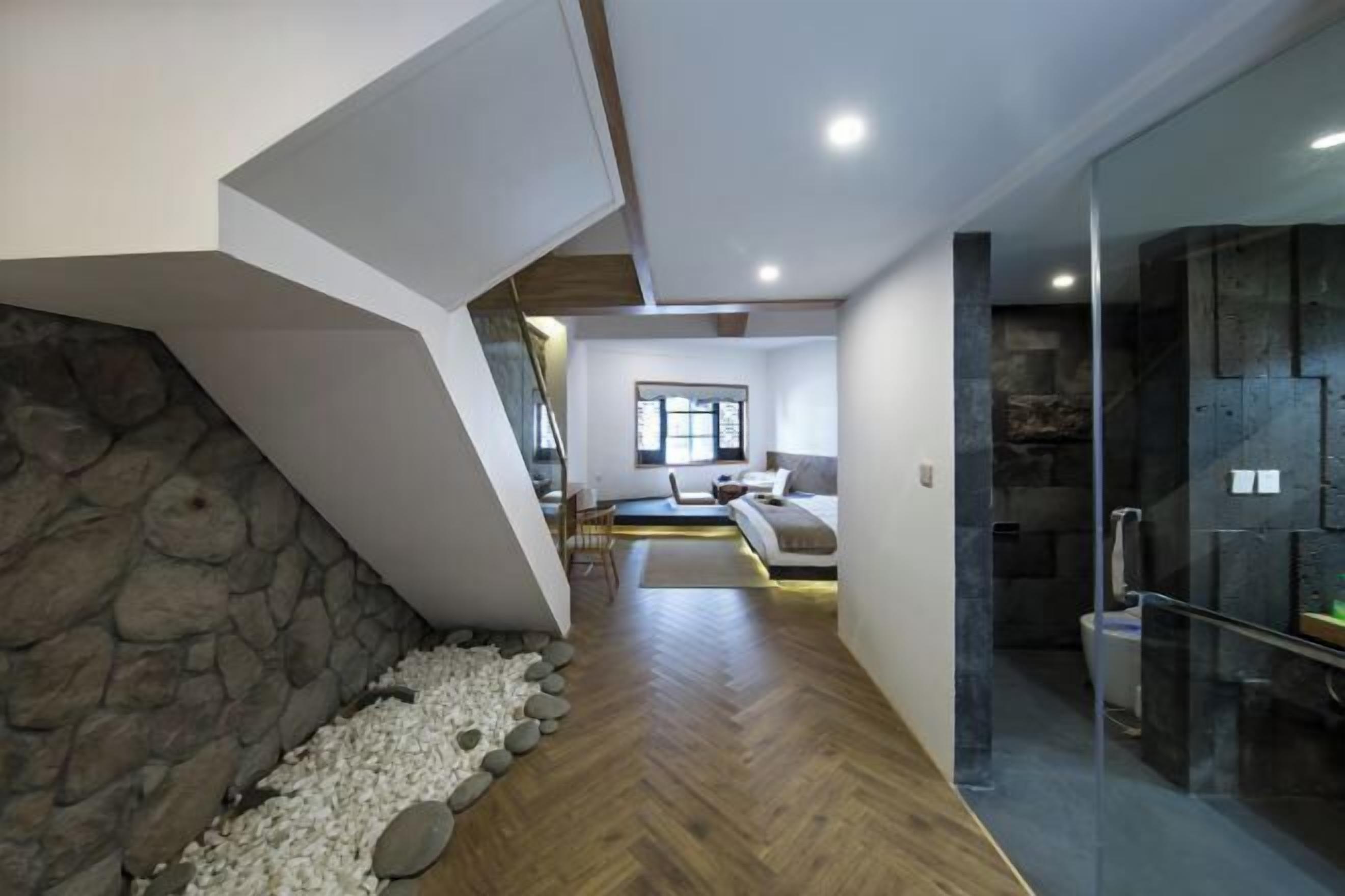 A modern interior with a stone wall, wooden flooring, a seating area with a sofa and chairs, and a glass-enclosed shower area.