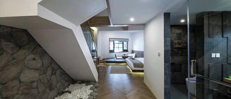 A modern interior with a stone wall, wooden flooring, a seating area with a sofa and chairs, and a glass-enclosed shower area.