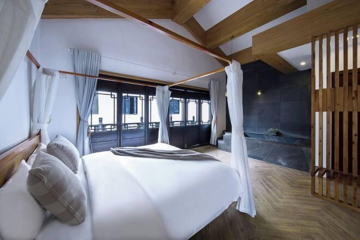 A bedroom with a bed, curtains, a view of a pool, and a stone wall.