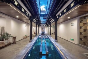 A hotel corridor with a central pool, wooden pillars, and a skylight.