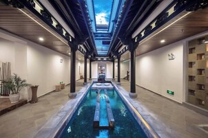 A hotel corridor with a central pool, wooden pillars, and a skylight.