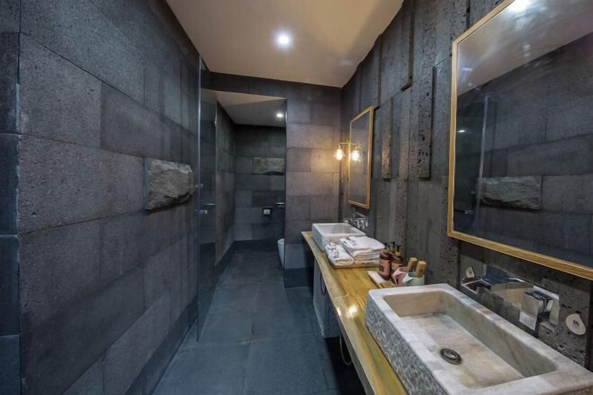 A modern bathroom with stone walls, a wooden vanity, two sinks, and a large mirror.