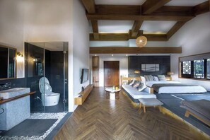 Un dormitorio moderno con una cama grande, un sofá, una mesita y un baño con inodoro y lavamanos.