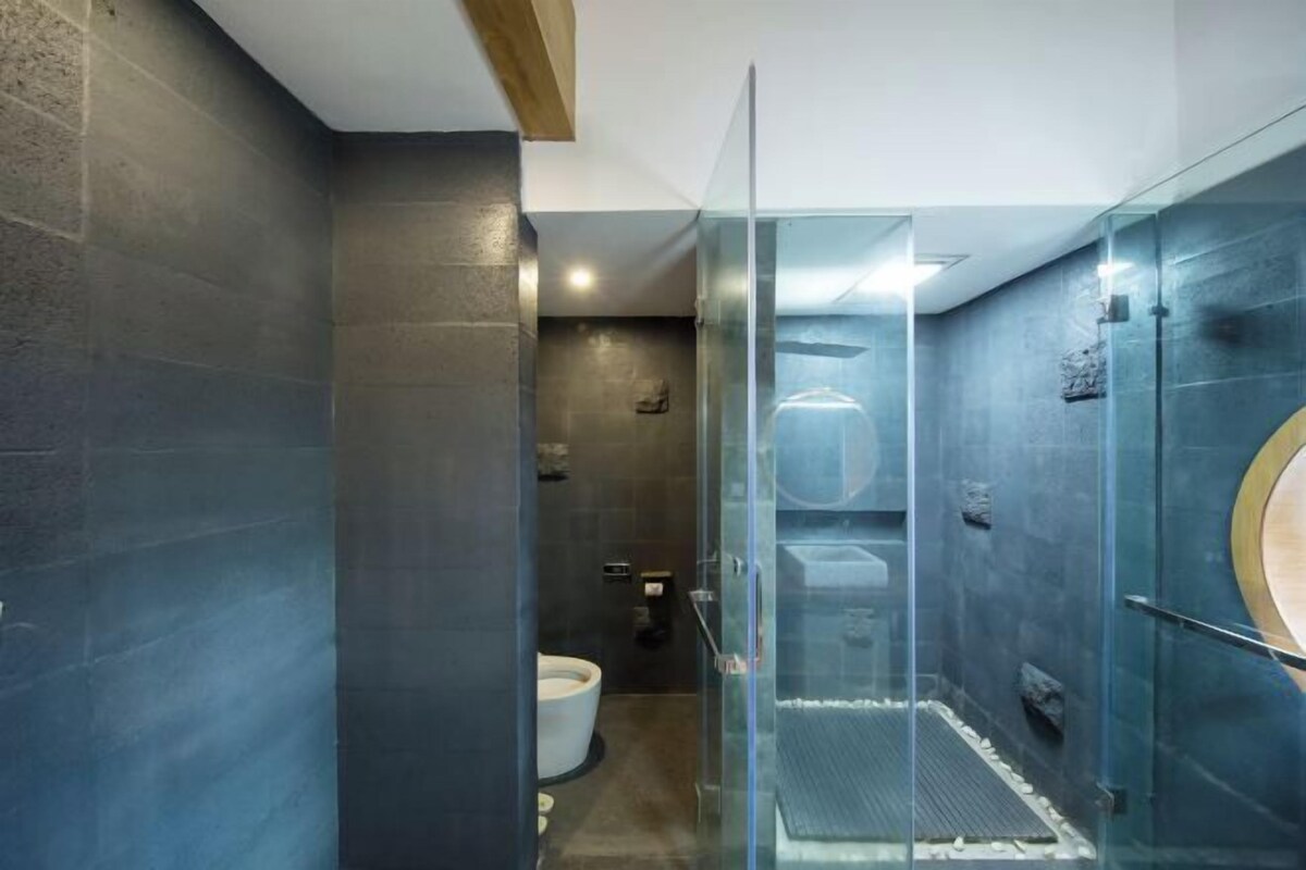 A modern bathroom with dark stone walls, a glass-enclosed shower, and a visible toilet.
