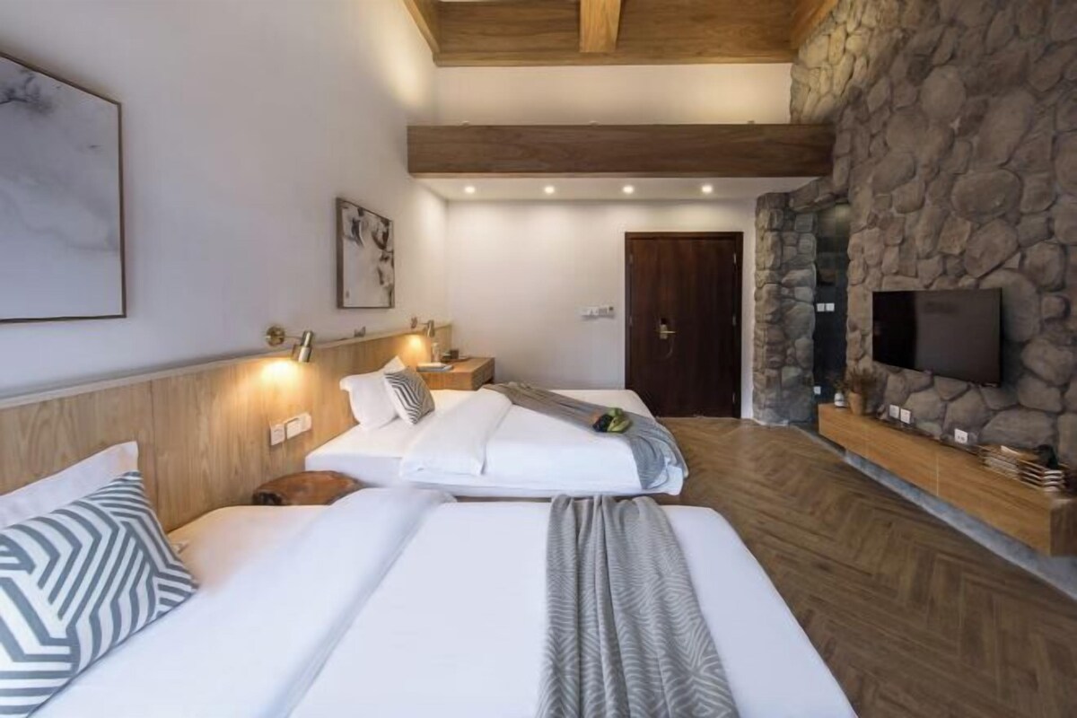 A hotel room with two beds, a stone wall, a TV, and a wooden ceiling.