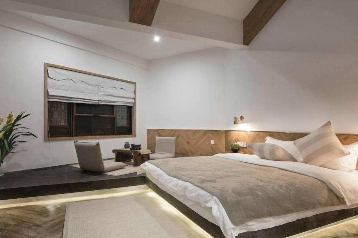 A modern bedroom with a bed, bedside tables, a nightstand, a window with curtains, and a potted plant.