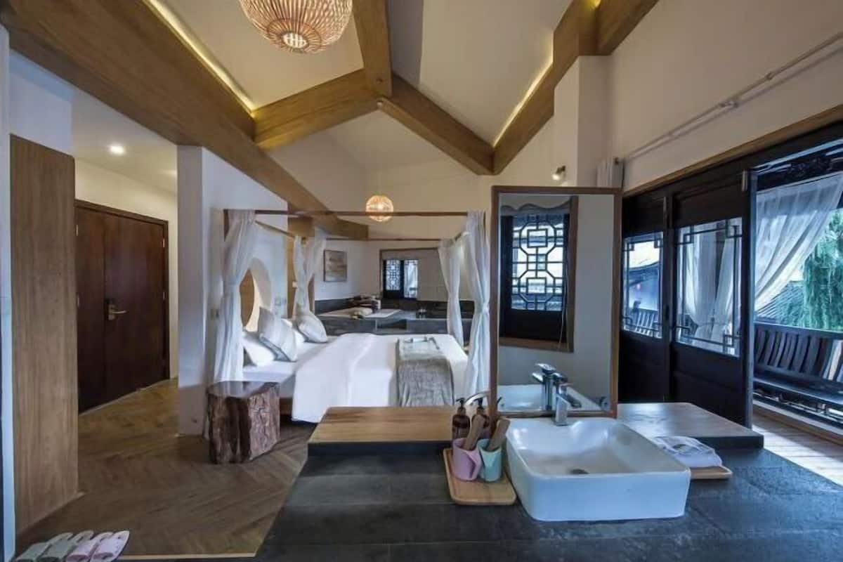 A bedroom with a large bed, a bedside table, a mirror, and a view of the outside.