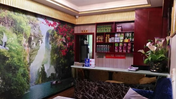 A reception area with a mural of a river and trees, a reception desk, a shelf with various products, and a blue sofa with a cushion. - Bazhong city home business hotel (Bazhong)