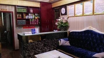 A reception area with a marble counter, a blue velvet sofa, and a shelf with various beverages.