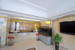 A hotel reception area with a marble counter, two red bar stools, a fish tank, a television mounted on the wall, and a potted plant. - Xingyi Satisfaction 168 Hotel (Xingyi)