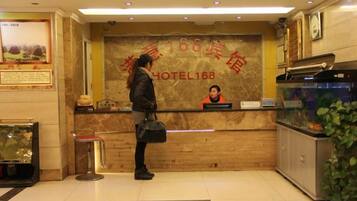 A hotel reception desk with a receptionist, a framed welcome sign, and a fish tank.