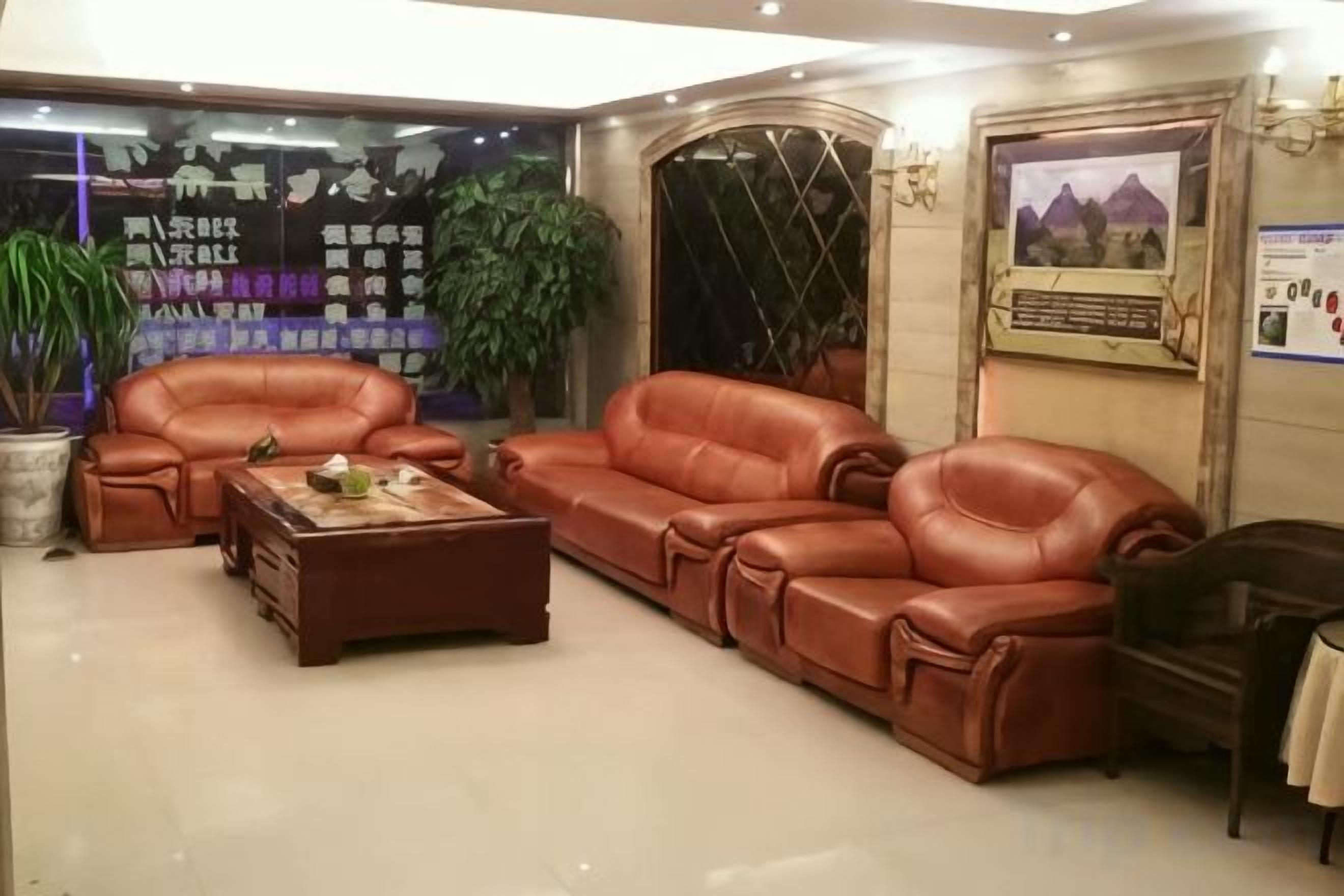 Una sala de estar con sofás de cuero, una mesa de centro y un sillón oscuro. Hay plantas en macetas y un cuadro en la pared.