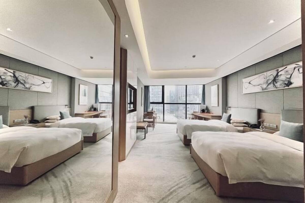 Une chambre d’hôtel moderne avec deux lits, un bureau et une grande fenêtre.