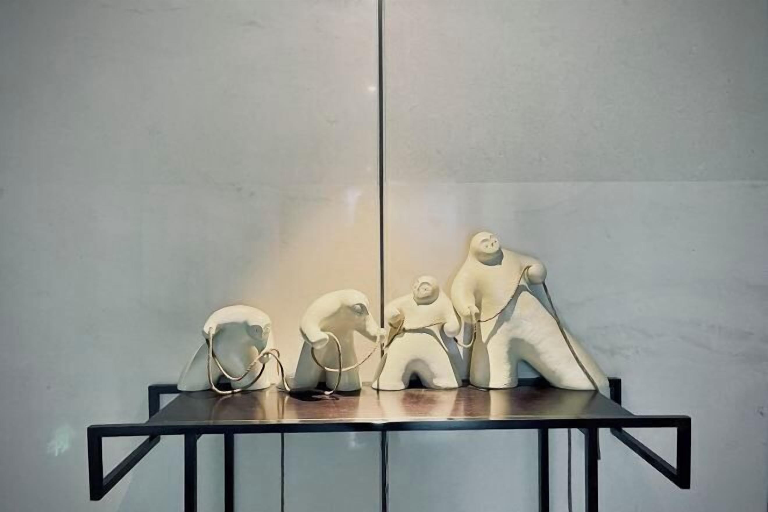 Una mesa con tres esculturas blancas frente a una pared lisa.