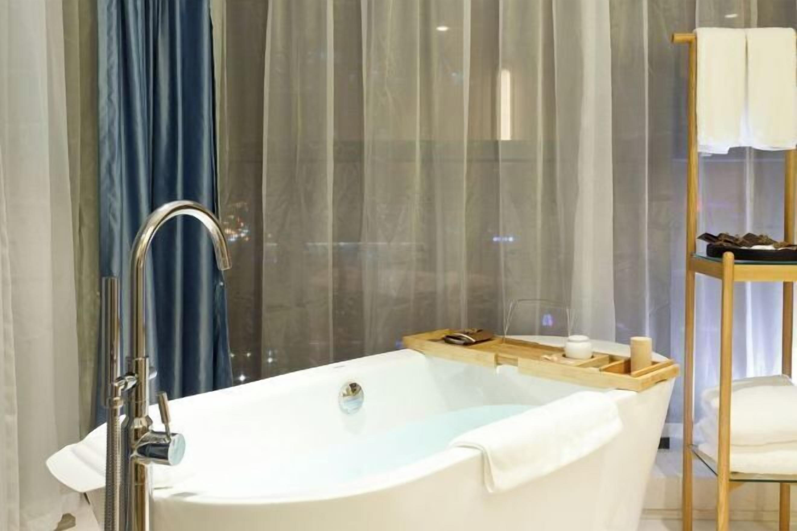 A modern bathroom with a freestanding bathtub, a wooden side table with toiletries, and a glass shower enclosure.