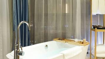 A modern bathroom with a freestanding bathtub, a wooden side table with toiletries, and a glass shower enclosure.