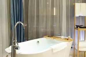 Un baño moderno con una bañera independiente, una mesita de madera con artículos de aseo y un box de ducha de vidrio.