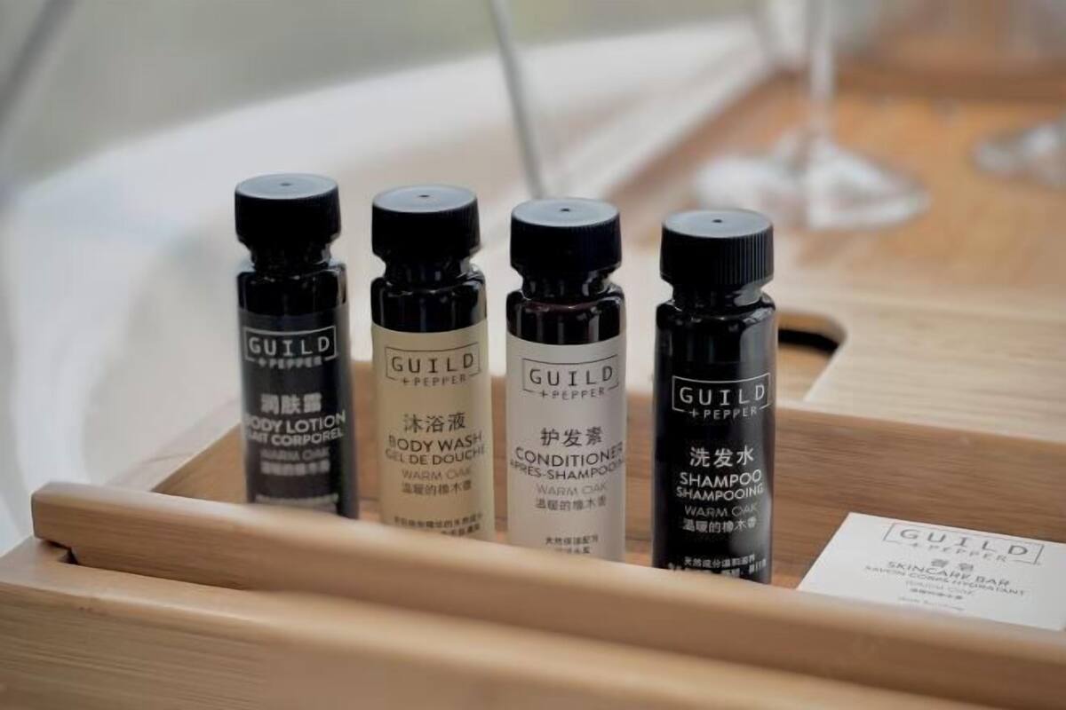 Quatre flacons de produits de soins corporels de la marque Guild + Pepper, présentés dans un plateau en bois.