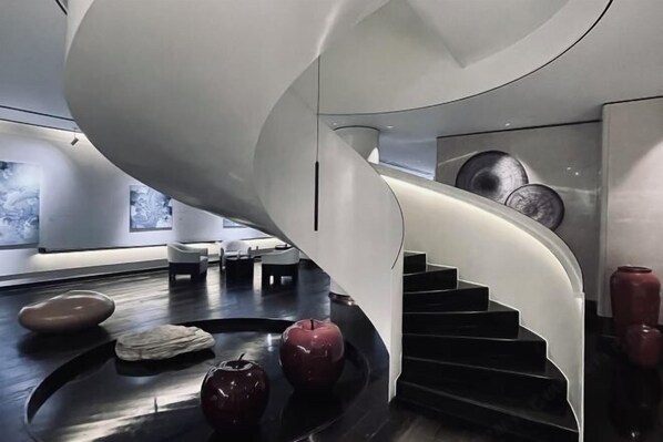 Ein modernes Interieur mit einer Wendeltreppe, einer Steinskulptur und einem roten Apfel auf dem Boden.