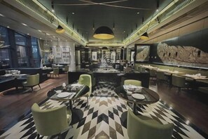 Interior moderno de restaurante con zona de comedor central, varias mesas y sillas.