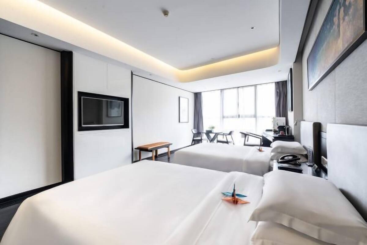Une chambre d’hôtel avec deux lits, une télévision, un bureau et une fenêtre avec des rideaux.