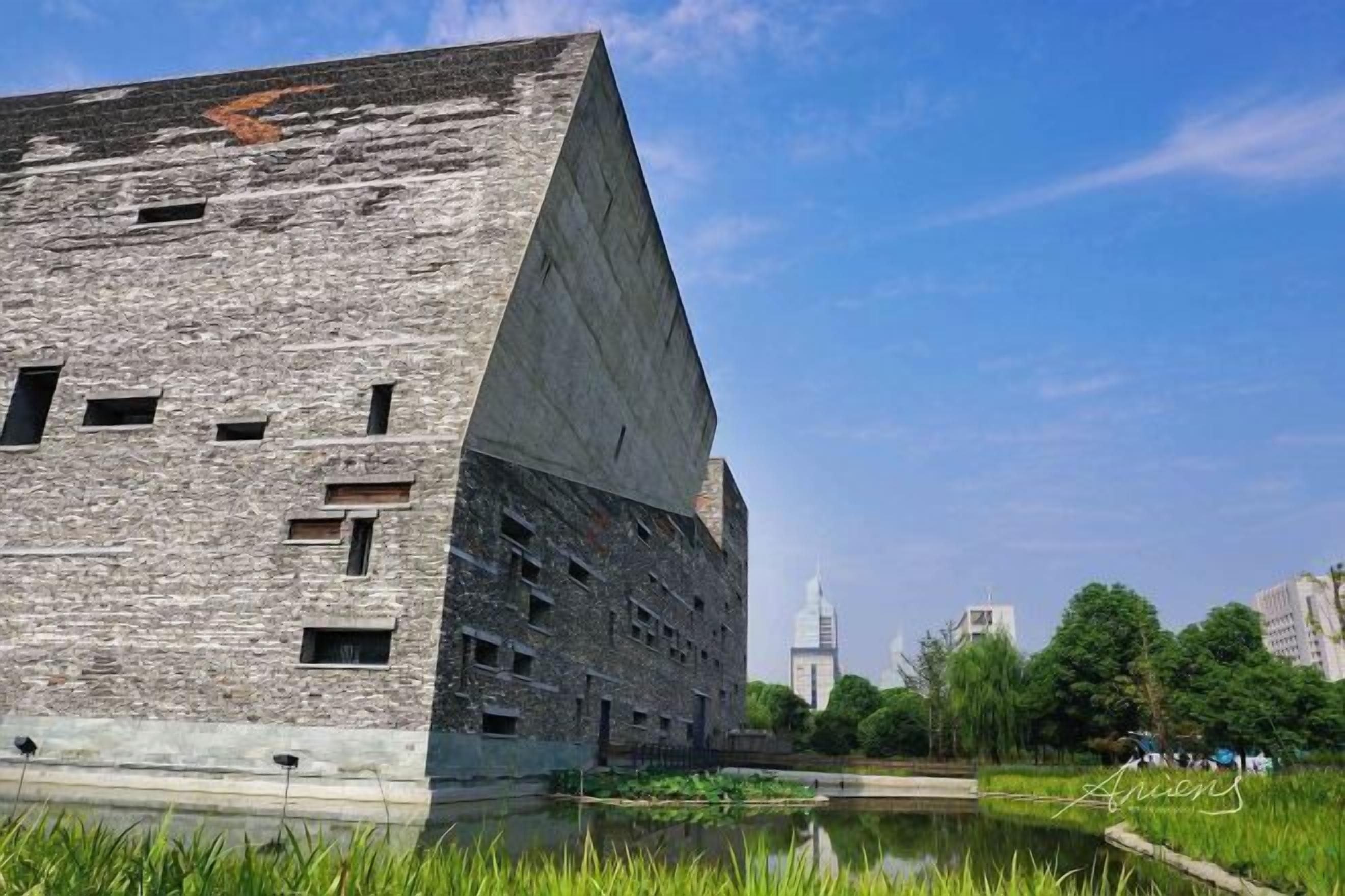 A modern building with a unique angular design, a pond in the foreground, and a clear sky.