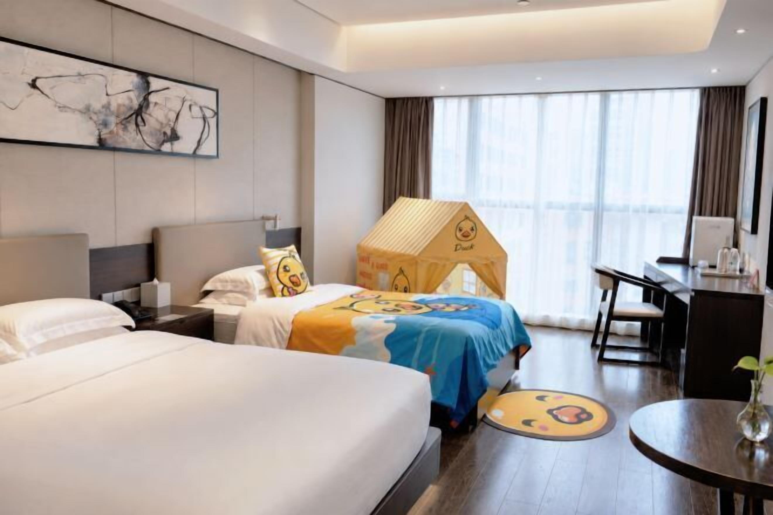 A hotel room with two beds, a desk, a chair, a round table, and a large window.