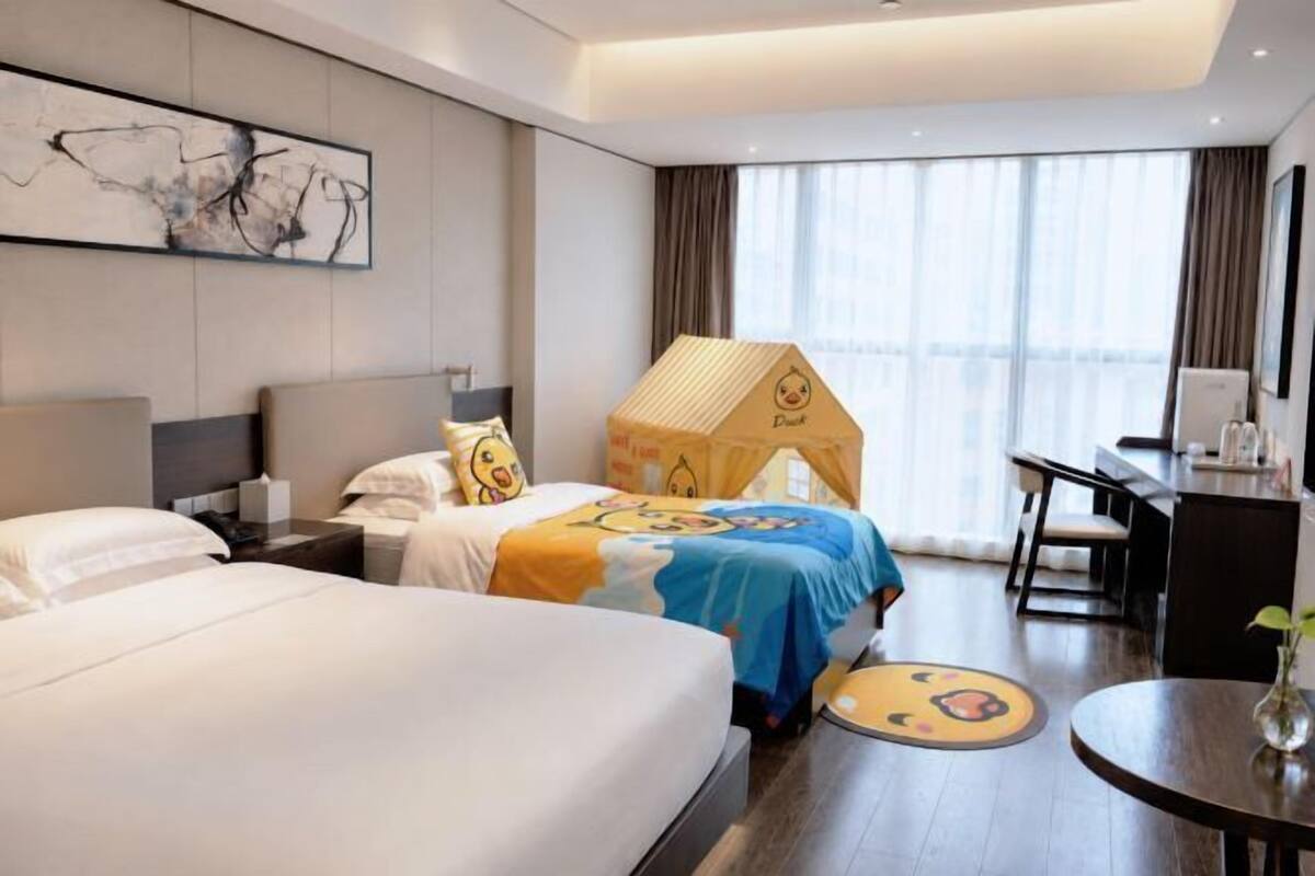 Une chambre d’hôtel avec deux lits, un bureau, une chaise, une table ronde et une grande fenêtre.