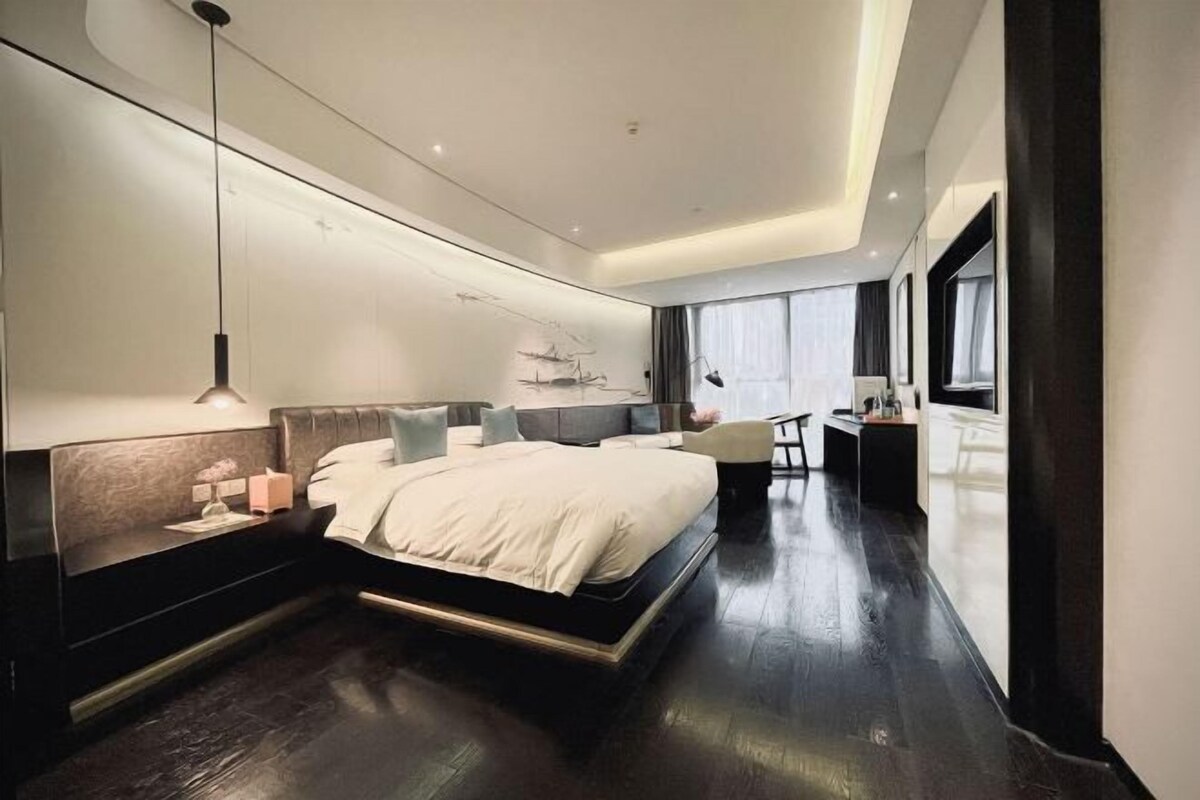 A modern bedroom with a large bed, bedside tables, a desk, and a chair.