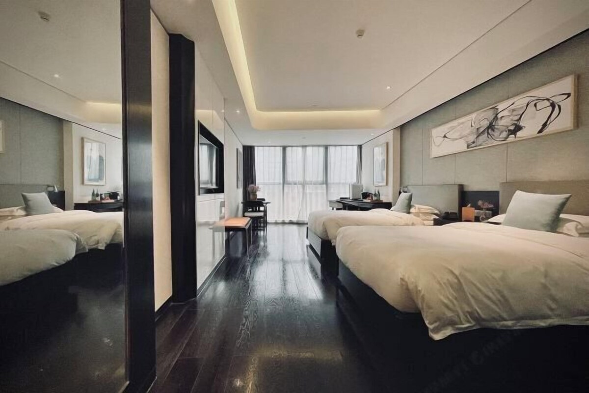 A modern hotel room with two beds, a desk, and a large window.