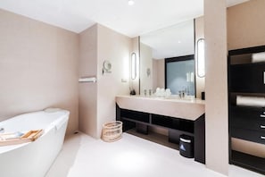 A modern bathroom with a large bathtub, a vanity with a mirror, and a black shelving unit.