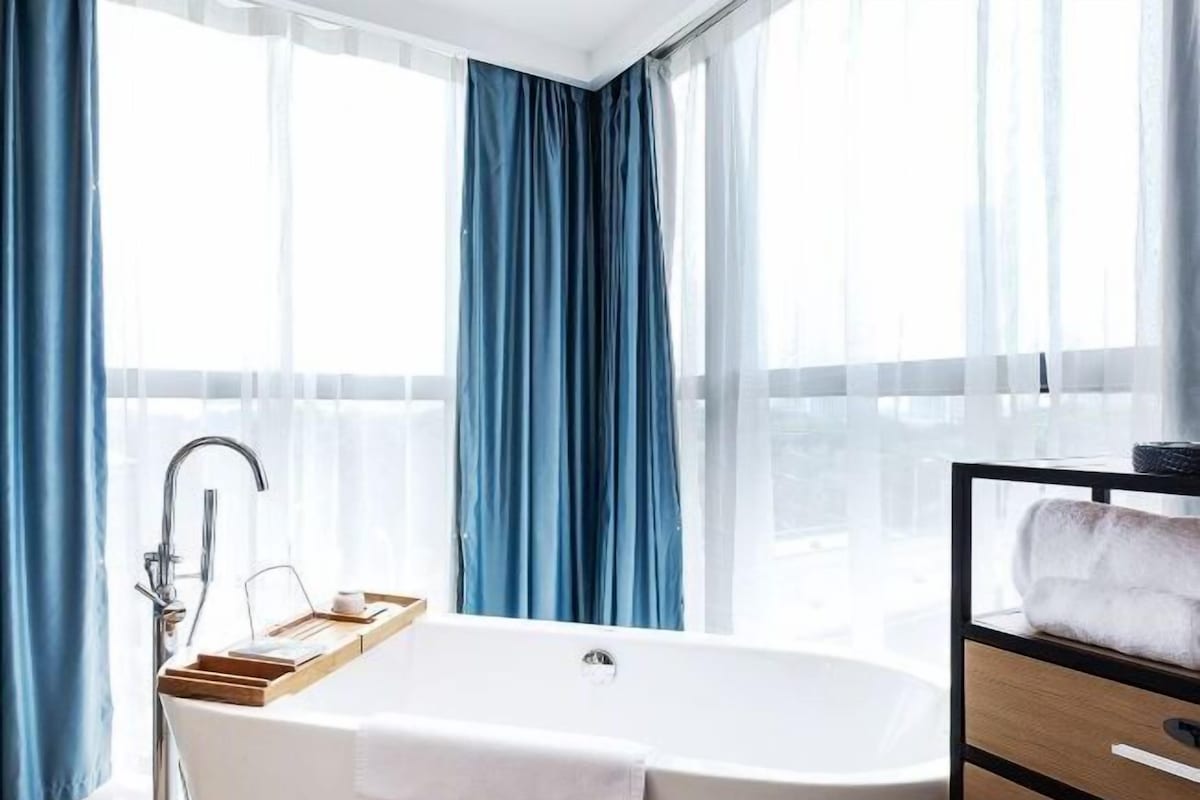 A modern bathroom with a freestanding bathtub, a glass shower enclosure, and a view of the city through large windows.