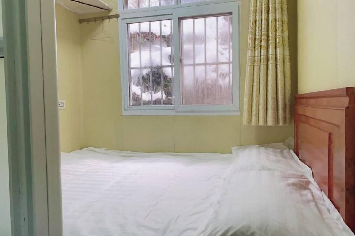 Una habitación con cama, ventana que ofrece vistas a un paisaje nevado y cortina.