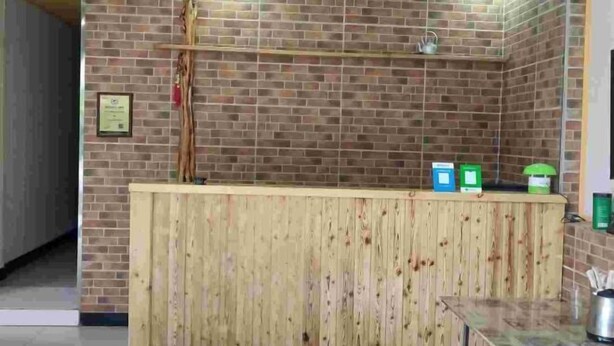 A reception area with a wooden counter, brick wall, and a small shelf with items. - Qixingshu Deshun Inn (Danjiangkou)