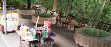 An outdoor dining area with tables and chairs, a table with beverages and snacks, and a food cart.