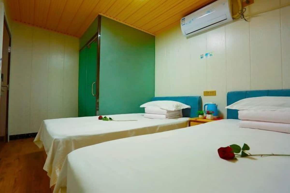 Habitación de hotel con dos camas, una pared verde, techo de madera y unidad de aire acondicionado.