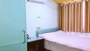 Et lille værelse med seng, natbord, garderobeskab og en klimaanlæg.