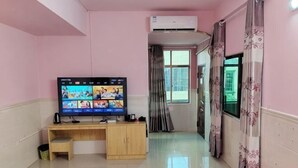 A room with a television on a wooden desk, a window with curtains, and an air conditioning unit. - longzhou hostel (Wanning)
