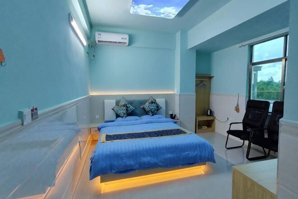 A modern hotel room with a bed, bedside tables, a desk, and a large window.